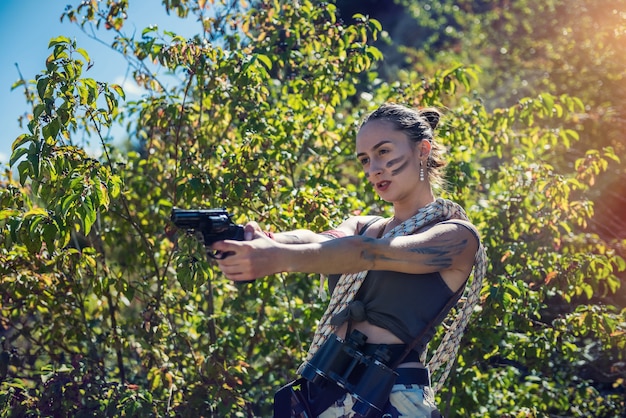 セクシーな女性モデルは、夏の屋外、軍のコンセプトで銃と短い布を着用します