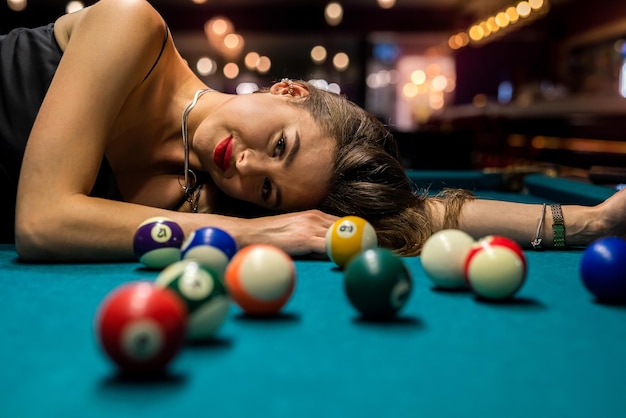 Sexy female pool player wear black dress lying on billiard table