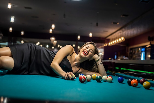 Sexy female pool player wear black dress lying on billiard table