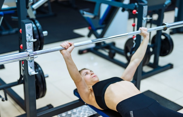 Sexy fit meisje liggend op speciale simulator en doet push-up oefening met barbell