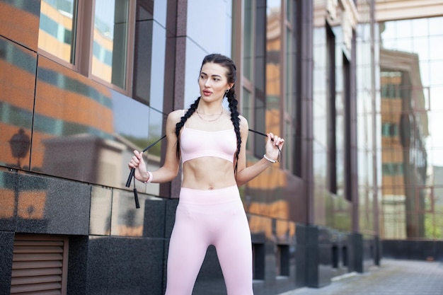 Sexy fit woman posing with a skipping rope in her hands on background of city building