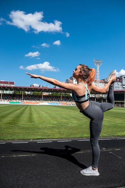 Sexy fitness vrouw maakt rekken en opwarmen voor een harde training in de buitenlucht, stadion