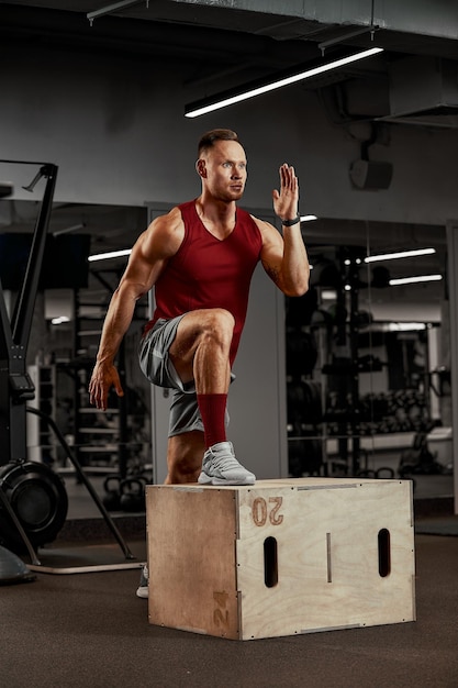 Sexy gespierde mannen met behulp van het platform voor zijn benen op een donkere kleurrijke achtergrond van sportschool.