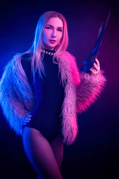 The sexy girl in a bodysuit and fur coat with a rabbit mask in the neon light