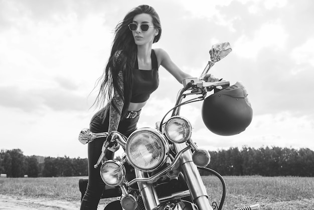 Sexy girl in a leather suit posing near a motorcycle at sunset. Travel concept. Mixed media