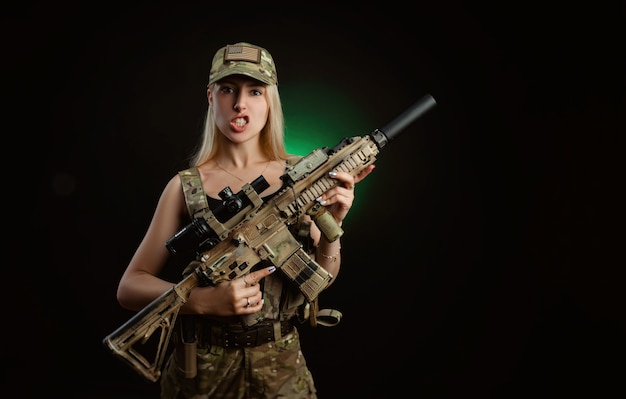 Una ragazza sexy in tuta militare softair posa con una pistola in mano su uno sfondo scuro