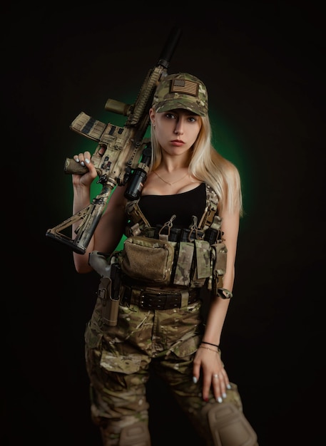 Una ragazza sexy in tuta militare softair posa con una pistola in mano su uno sfondo scuro