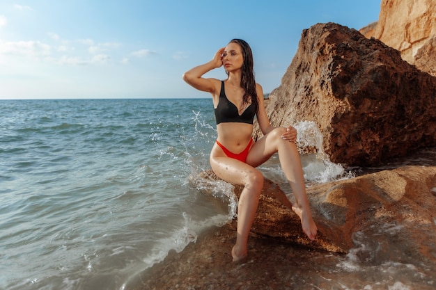 La ragazza sexy in costume da bagno rosso è seduta sulla spiaggia