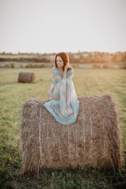 Ragazza sexy in biancheria intima in posa su un mucchio di fieno in estate al tramonto nella natura. aggiunto l'effetto di una piccola grana della pellicola