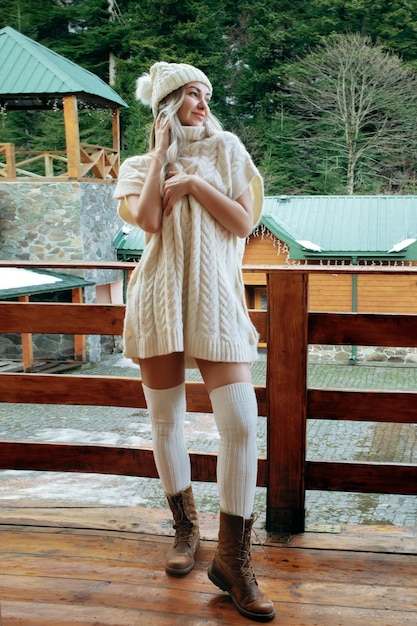 A sexy girl in a white sweater and stockings on the balcony admires the beauty of nature wool
