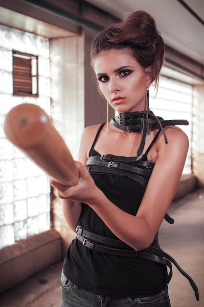 Photo sexy girl with a leather belt on the neck holds a baseball bat in his hands.