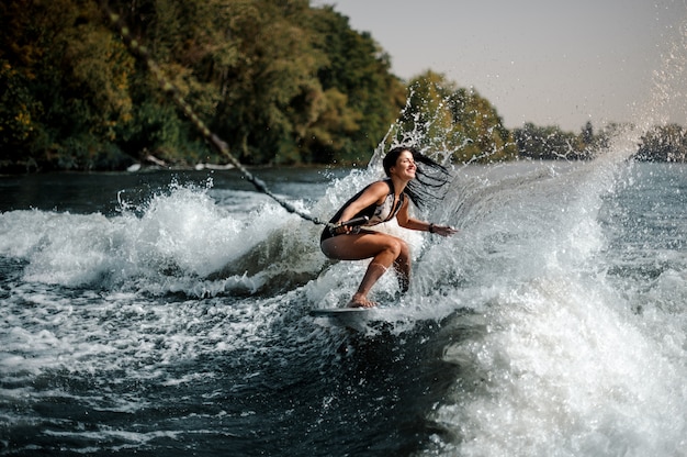 Sexy glimlachende donkerbruine vrouw die aan boord van het blauwe water surft