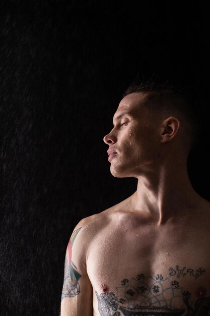 Sexy healthy tattooed man with water drops on his body Naked torso fashion male studio portrait