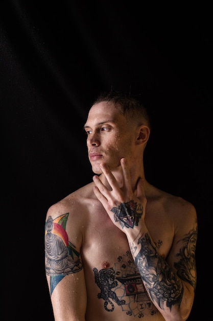 Sexy healthy tattooed man with water drops on his body Naked torso fashion male studio portrait