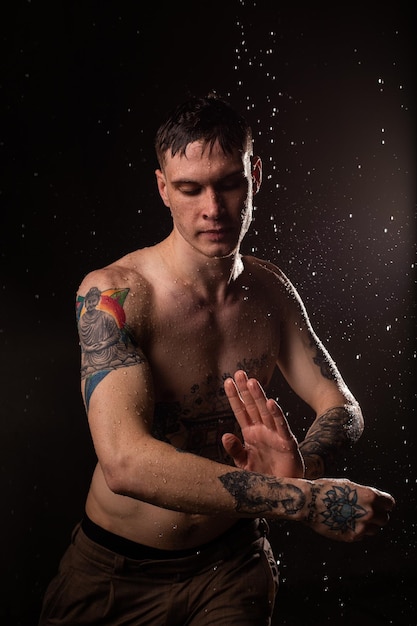 彼の体に水滴を持つセクシーな健康的な入れ墨の男裸の胴体ファッション男性スタジオの肖像画