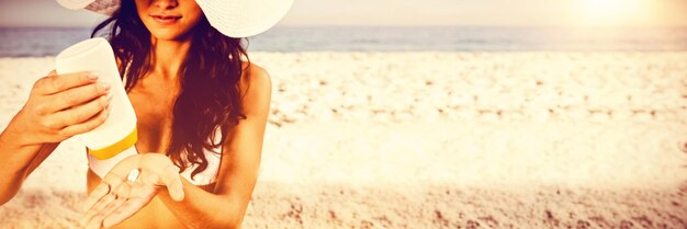 Sexy jonge brunette op het strand die haar lichaam verzorgt en zonnebrandcrème aanbrengt