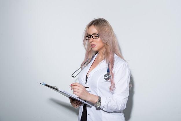 Sexy jonge dokter in een witte medische jurk schrijft in de kaart van de patiënt