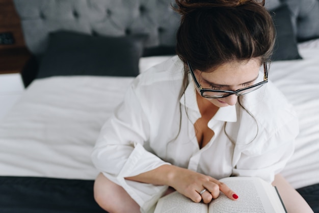 Sexy jonge vrouw die een boek op haar bed binnen met wat zichtbaar splijten leest