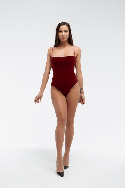 Sexy jonge vrouw draagt rode bodysuit en schoenen met hoge hakken staande op een witte background