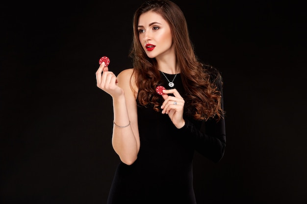 Sexy krullend haar brunette poseren met chips in haar handen poker concept zwarte achtergrond