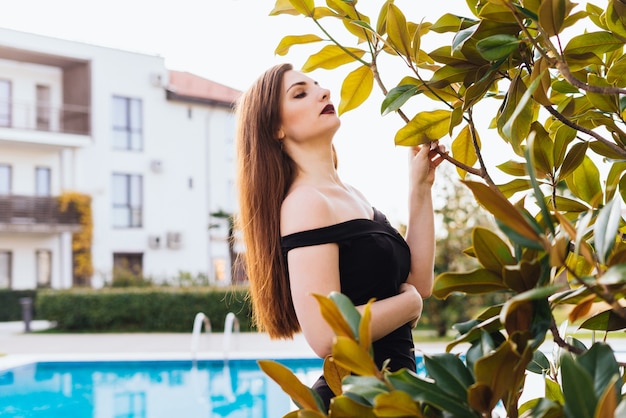 Sexy langharig meisje in een zwarte jurk lopend door de tuin, genietend van een rijk leven
