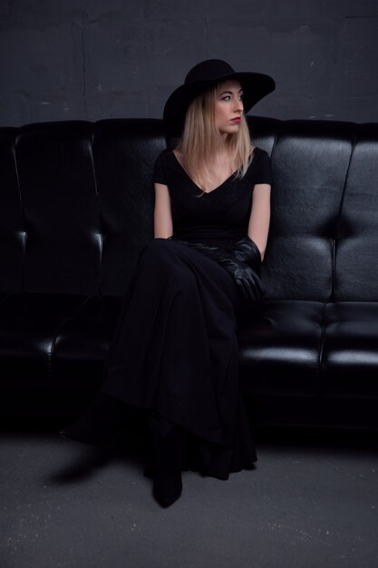 Сексуальная длинноволосая блондинка с ярким макияжем в черной шляпе и стильном элегантном вечернем платье