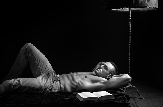 Sexy man in de slaapkamer knappe shirtloze jonge man die een boek leest in bed.