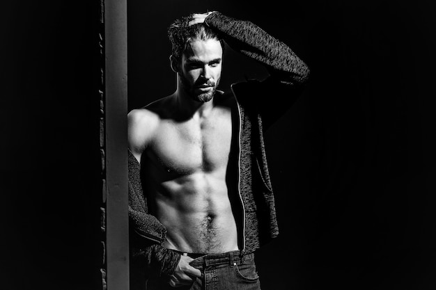 Sexy man with muscular bare torso in studio on black and brick wall background, copy space