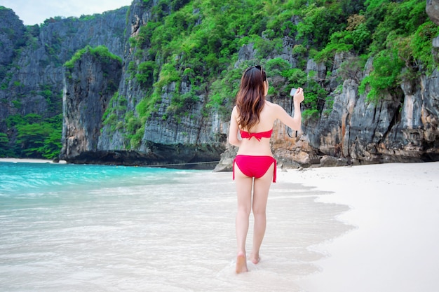 Sexy meisje draagt een rode bikini en neemt een foto op het strand.