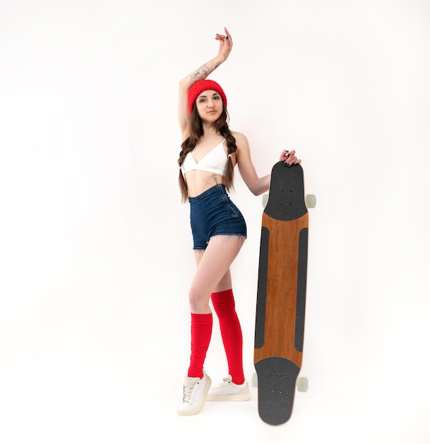 Sexy meisje in een modieuze rode hoed met een longboard op een witte achtergrond