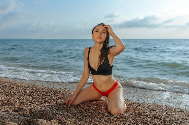 Sexy meisje in een rood zwempak zit op het strand