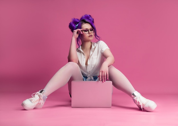 Sexy meisje met bril en paars haar met een laptop op een roze achtergrond