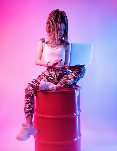 sexy meisje met vlechten dreadlocks op haar hoofd in neonlicht met een laptop op een lichte achtergrond kopiëren en plakken