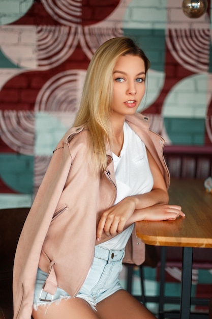Sexy mooi Amerikaans meisjesmodel in een roze jasje en denimborrels die in een koffie zitten