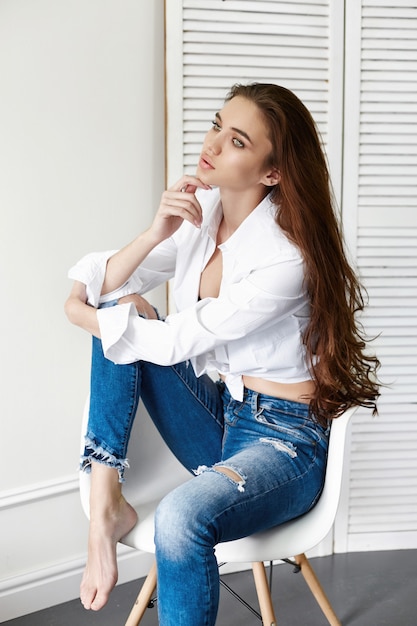 Sexy mooi meisje in jeans wit shirt zittend op een stoel