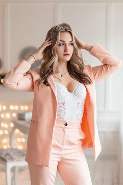 Sexy mooie vrouw in een modieus pak met een blazer en witte kanten lingerie met weelderige borsten staat in een schoonheidsstudio