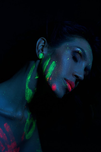 Sexy Nude woman in neon light, UV paint on the woman face and body. Perfect figure and Breasts of a woman, beautiful hair