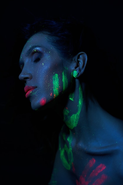 Foto sexy donna nuda in luce al neon, vernice uv sul viso e sul corpo della donna