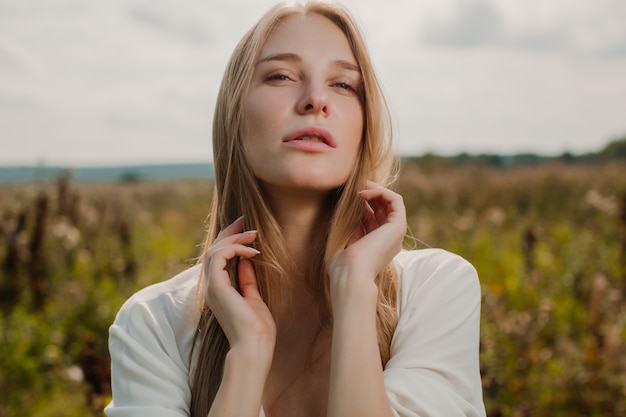 Sexy nymph with bare shoulders stands on the background of a green meadow.