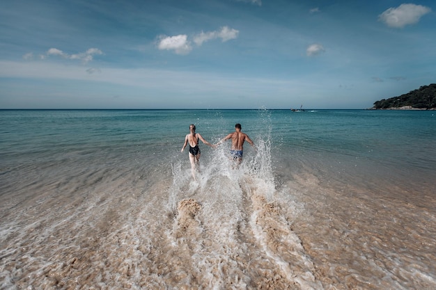 Sexy paar in het water. Grote golven van de zee. Mooie blonde in zwarte zwembroek met lang haar en een man zijn op vakantie. Phuket. Thailand.