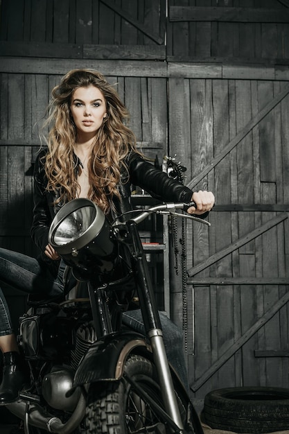 Sexy pretty biker in leather jacket sitting on vintage motorcycle