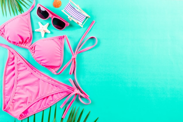 Sexy roze bikini, zonnebril en palmbladeren op lichtgroene achtergrond. Zomer of vakantie concept.