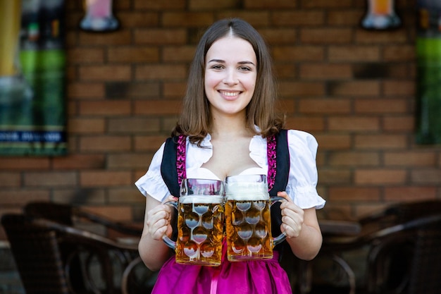 Foto donna russa sexy con un vestito bavarese che tiene in mano tazze di birra