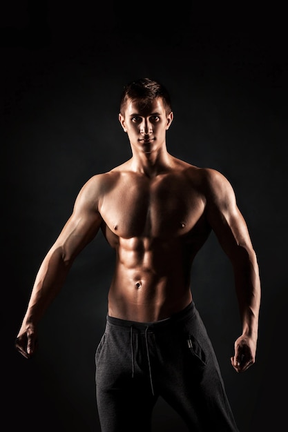 Sexy shirtless bodybuilder posing and looking at camera on black background. Extreme strength, muscles and fitness..