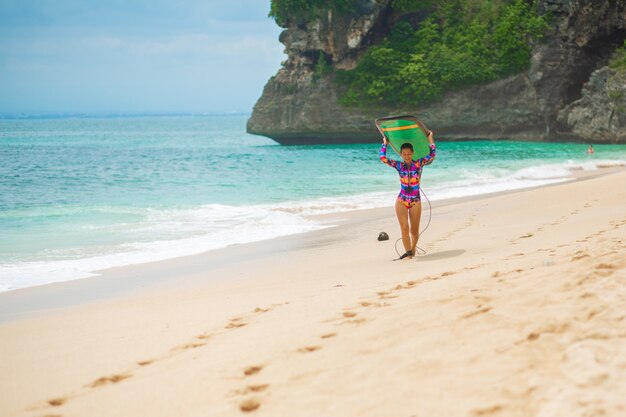 Sexy slim girl with surf board on tropical sand beach.