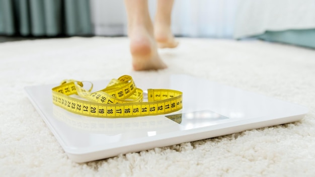 Photo sexy slim woman weighting on scales and walking on soft carpet in bedroom concept of dieting