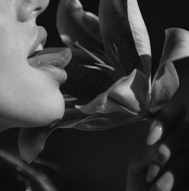 セクシーな舌のセクシーな女性は、デイリリー オリエンタル ハイブリッド ユリやヒッピースタルムと花の女性の唇をなめます