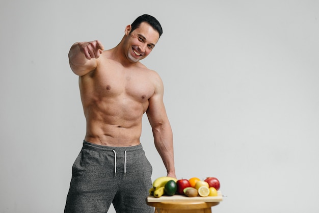 Sexy vegan guy with a naked torso posing in the Studio next to fruit. Diet. Healthy diet