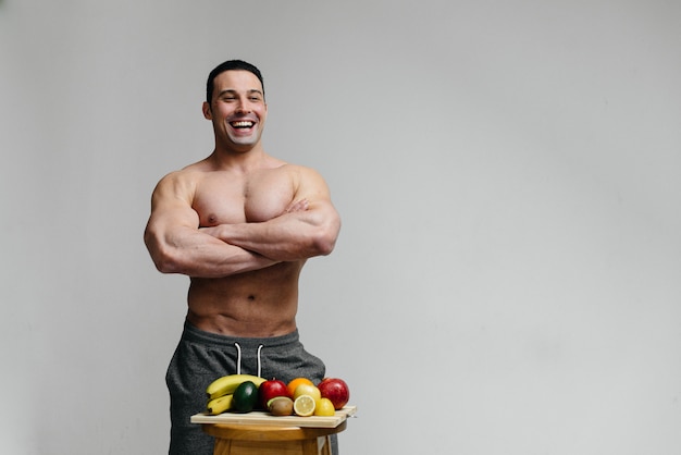 Sexy vegan guy with a naked torso posing in the Studio next to fruit. Diet. Healthy diet