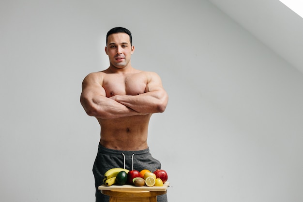 Сексуальный веганский парень с голым торсом позирует в студии рядом с фруктами Рацион питания. Здоровая диета